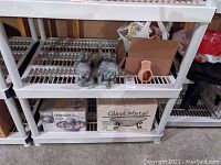 Shelf with two gray resin figurines, boxed Envirascape fountain and glass & metal stand, small pottery candle holders, and other items in background