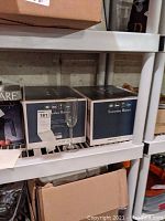 Two cardboard boxes labeled 'Everyday Basics' each containing 12 wine glasses, with one clear wine glass visible outside the boxes.