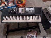 Top-down photo showing Yamaha PSR-330 keyboard on stand with tutorial materials below and basket of cables nearby