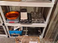 Shelf showing orange pumpkin bake pan, two muffin pans, grater, and popcorn maker.