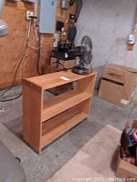 Light wood bookshelf with two shelves in a basement setting, visible wear and dust.