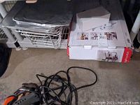 Photo showing stacked metal chafing dish with lid and stand, box labeled for chafing dish and baskets, with some cables on floor