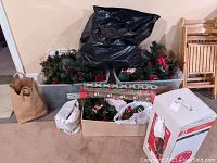 Wide photo showing multiple Christmas decorations including wreaths, wrapping paper rolls, gift tags, and pre-lit snowman topiary in white box.