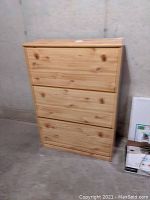 Front view of closed three-level pine shoe cabinet against concrete wall.