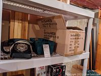 Black vintage rotary telephone on a shelf showing dial and handset with plastic label cover missing.