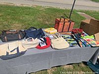 Shows overall collection of 14 bags on a table outside, including large multi-compartment tote, canvas totes in beige and blue, colorful shopping bags, and various small purses and pouches.