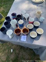 Table with 20 assorted coffee mugs and creamers, various colors and patterns visible