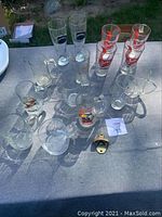 Overview photo showing all beer glasses, mugs, and bottle opener on table outdoors.