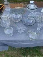 Crystal serving pieces including decanter, bowls, trays, cake plate, vase, sugar and creamer arranged on table.