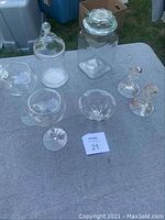 Full overview of all glass items including canisters, bowls, candlesticks, and stemmed glasses on gray tablecloth outdoors.