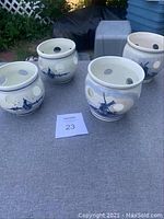 Set of four white ceramic candleholders with Delft blue hand-painted Dutch windmill and floral designs, featuring large ventilation holes around the round body and near the top rim. Each has a bulbous shape and glossy finish.