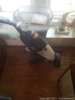 Oreck Steamer carpet cleaner upright unit positioned on floor near window, showing full body angled to the side with power cord loosely coiled.