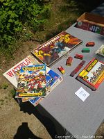 Overview photo showing Warhammer 40,000 manuals (Codex Imperialis), Waterloo game manual, Pro Football board game, and several small toy trucks on table.