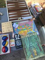 Photo of wooden backgammon board, juggling balls, educational puzzles, children's books, and Kitty Cat clock on table with boxes visible next to table.