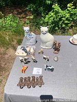 Table setup with various animal figurines and cast iron key hook arranged on gray cloth outdoors.
