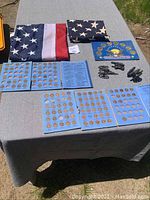 View of entire lot on table including two folded American flags, coin folders with Lincoln cents, presidential collector coin set, miniature cannons and informational folder.