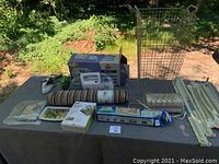 Photo of household items laid on black tablecloth including two travel irons, metal hamper, rolled mat, vacuum seal bags, rods, and Bissell spot lifter in box.