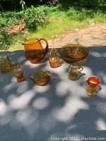 Overview of all yellow Depression glass items on display outdoors on cloth surface with greenery background.