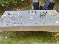 Overview of assorted pins, belt buckles, jewelry items laid on grey cloth outdoors