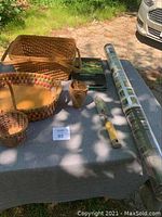 Photo of large, medium, and small woven baskets, hand spade, roll of biodegradable ceiling pots, and WeedBlock garden fabric on table.