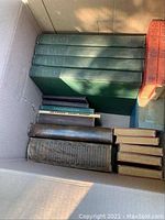 Box with several vintage books including green hardcover volumes and leather bound books, additionally some smaller red and orange red books visible.