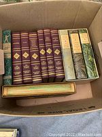 Box containing multiple volumes of classic literature including Harvard Classics and other classic collections, with some books in decorative slipcases.