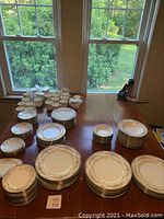 Overview of entire china set spread across dining table showing stacks of dinner, salad, bread plates, bowls and cups.