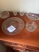 Various crystal pieces including sugar bowl, creamer, bowls, cake plate and serving dish arranged on wooden cabinet.