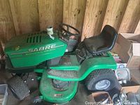 Front side view of lawn tractor with black seat, steering wheel, and green metal body.