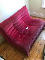 Front left angle view of red velvet Togo love seat showing channel tufting and minor seat wear.