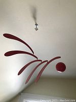 Full view of the mobile hanging from ceiling showing red sphere and black teardrop-shaped blades