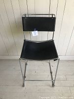 Front view of the stool showing chrome frame, black leather seat and backrest with tag attached