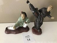 Both mud figurines viewed from front showing poses and colors