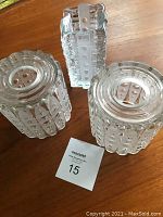 Two round textured glass pendant shades and one rectangular textured glass vase on wooden surface.