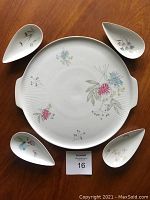 Serving set arranged with large round plate in center and four teardrop bowls positioned around it, showing floral designs on white porcelain.