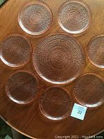 Image showing all eight vintage art glass plates with textured shell design arranged on wooden surface. One large 12-inch plate surrounded by seven smaller plates about 7.75 inches each, highlighting detailed rippled pattern and translucency.