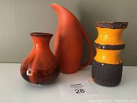 Three vintage orange ceramic pieces: a shiny Laurentian Art Pottery vase with dark accent glaze, an orange matte finish pitcher with elongated spout and handle, and a textured banded Blue Mountain Pottery vase with chips.