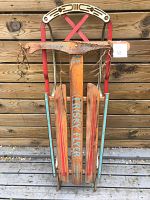 Front view of the vintage Preston Frisky Flyer sled showing wooden runners, T-bar handle with painted wings and red metal frame.