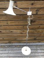 Full view of the vintage floor lamp showing the adjustable arm and flared white lampshade against a wooden fence background.