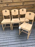Front and side view of four vintage wooden chairs arranged indoors, showing circular cutout backs and raw wood surface.