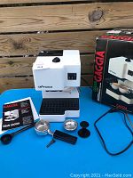 Front-left angle view of white and black Gran Gaggia machine on blue table with accessories and original box.