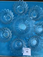 Top-down view of all eight clear art glass flower-shaped bowls arranged on blue surface, showing the scalloped petal edges with textured glass, one large and seven smaller bowls.