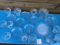 View of entire Dansk collectible art glassware set including plates, bowls, and vases arranged on a blue table surface.