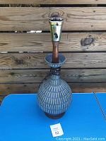 Full front view of midcentury pottery lamp showing bulb fixture, wooden segment, pattern on pottery base, and identification tag.