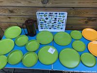 Overview of all items including green plates, bowls, brown pitcher, and fish design tray arranged on a blue table against wood wall.