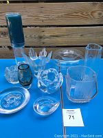 Full view of all ten glass pieces arranged on a blue surface, showcasing shapes, colors, and textures.