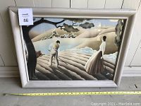 Framed vintage farm scene artwork showing man and woman by plowed fields with houses in distance, in wooden frame