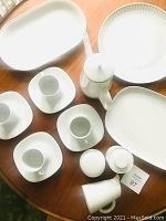 Top view photo showing four cups with saucers, small pitcher, sugar/salt cellars, creamer, and teapot on wooden table
