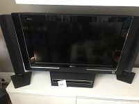 Front view of large Sony Bravia TV with integrated woofer in stand and two black companion speakers on stands.