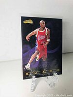 Front of Kobe Bryant basketball rookie card with player in red Lakers uniform, number 32, on clear plastic stand.